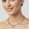 Woman wearing a gold necklace with charms on a plain background