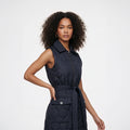 A woman modeling a sleeveless quilted navy puffer vest with a front zipper, collar, and matching tie belt, photographed against a clean light gray studio background.