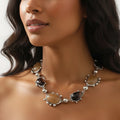 Woman wearing a silver necklace with dark gemstones on a neutral background