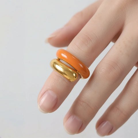 Hand wearing two rings, one orange and one gold, on a light gray background