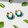 Gold hoop earrings with green beads on a white plate with greenery in the background