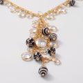 Gold-tone statement necklace with clear faceted crystal drops and black-and-white striped shell beads, photographed on a clean white background.