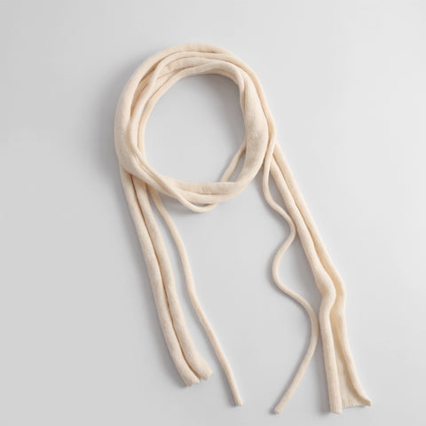 A long cream-colored knit scarf with long, thin tails, arranged in a loose loop on a light gray background.