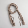 A textured, fuzzy knit scarf in a light taupe-beige color, styled in a loose loop on a clean, light gray background.