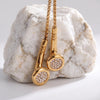 Gold slider necklaces with earbud-shaped pendant embellished with small clear stones, displayed on a light gray surface against a rock.