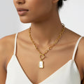 Woman wearing a gold chain necklace with a pendant on a plain background