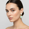 Woman wearing a gold earring with a turquoise stone on a neutral background