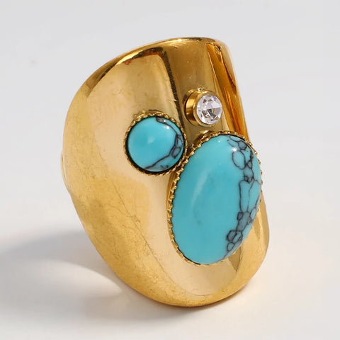 Gold ring with turquoise stones and a clear gemstone on a light gray background