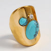 Gold ring with turquoise stones and a clear gemstone on a light gray background