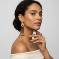 Woman wearing gold earrings and a ring on a plain background
