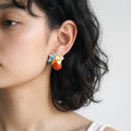 A close-up of a woman's ear wearing a colorful cluster stud earring with small pastel blue, yellow, white, and orange beads.